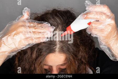 une femme applique du colorant aux racines de ses cheveux peint sur des cheveux gris. Banque D'Images