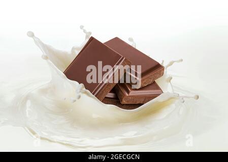 Morceaux de chocolat tombant dans le lait éclaboussant sur fond blanc Banque D'Images