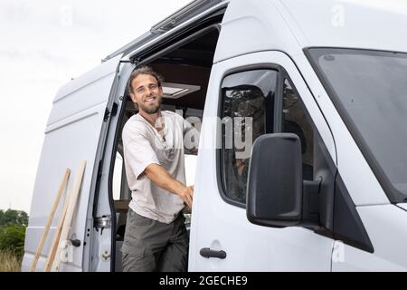 Homme souriant debout sur la porte d'une camionnette Banque D'Images