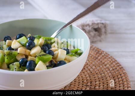 Un bol de salade de fruits à base de kiwis, de bleuets et de bananes servi avec une cuillère isolée sur une table de cuisine Banque D'Images