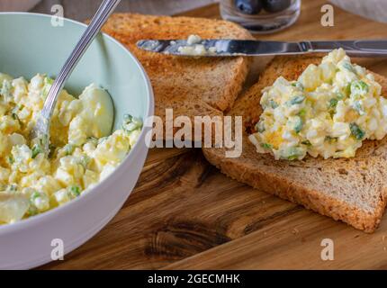 Salade d'œufs à faible teneur en gras, au fromage cottage, œufs durs et hachés et ciboulette servis avec du pain grillé sur une planche de bois. Repas riche en protéines Banque D'Images