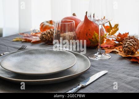 Le dîner d'Halloween et de Thanksgiving décoré de feuilles sèches d'automne, de citrouilles, de cônes et de guirlande sur une nappe en lin gris. Gros plan. Banque D'Images
