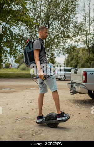 Homme avec un sac à dos sur un skateboard motorisé à une roue sur le trottoir Banque D'Images