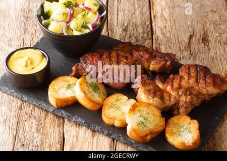 Col de porc allemand Grilled Schwenkbraten avec salade de pommes de terre, moutarde et toasts gros plan dans le plateau d'ardoise sur la table. Horizontale Banque D'Images