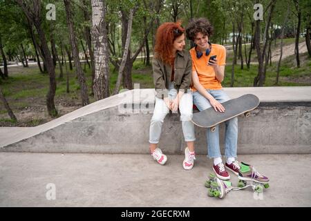 jeune patineur utilisant un smartphone tout en étant assis avec un ami à la frontière dans le parc Banque D'Images