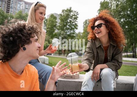 femme excitée dans des lunettes de soleil donnant un cocktail rafraîchissant à l'homme à l'extérieur Banque D'Images