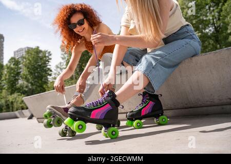 femme en lunettes de soleil nouant des lacets sur le patin à roulettes près d'un ami dans le parc Banque D'Images