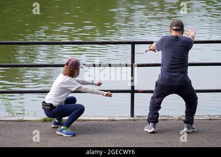 Un aide aide aide un homme ayant des problèmes de santé à faire sa routine d'étirement. Dans un parc à Queens, New York. Banque D'Images