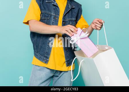 Vue rognée de l'homme mettant boîte cadeau dans un sac de shopping isolé sur bleu Banque D'Images