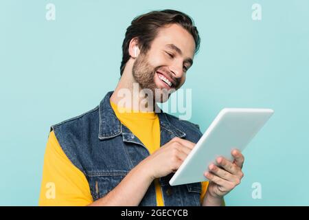 Jeune homme dans un écouteur utilisant une tablette numérique isolée sur bleu Banque D'Images