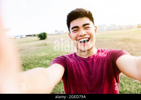 Un jeune homme asiatique heureux prenant un portrait de selfie avec un téléphone portable dans le parc de la ville Banque D'Images