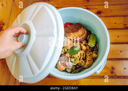 Les déchets d'aliments biologiques dans le seau à poubelle avec couvercle à la maison sur le sol à composter. Banque D'Images