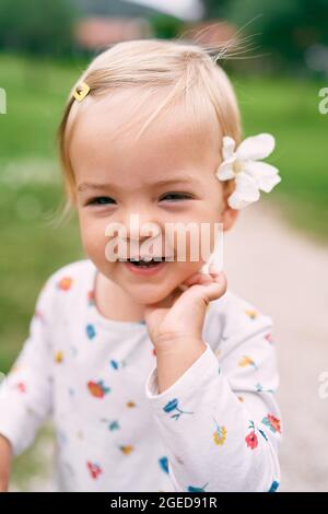 Une petite fille souriante avec une fleur d'oléander derrière son oreille se tient sur la pelouse. Portrait Banque D'Images