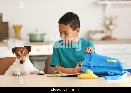 Mignon petit garçon avec chien drôle mettant son déjeuner d'école dans le sac Banque D'Images