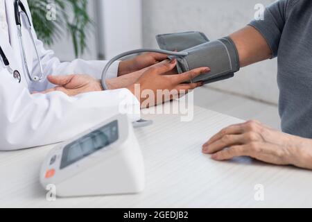 Vue rognée d'un médecin afro-américain portant un tonomètre sur le bras du patient Banque D'Images