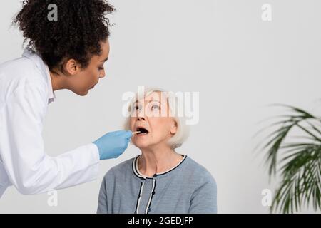 Médecin afro-américain en gants de latex vérifiant la gorge d'un patient âgé Banque D'Images