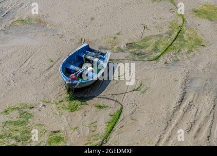 Petit bateau à rames bleu coincé dans la boue à marée basse dans le port de Folkestone. La marée montante reflottera le bateau pour le rendre à nouveau accessible. Banque D'Images