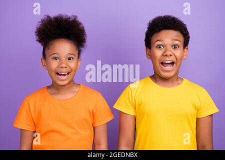 Photo de deux jeunes afro petit enfant heureux sourire positif surpris choqué surprise nouvelles isolées sur fond violet couleur Banque D'Images