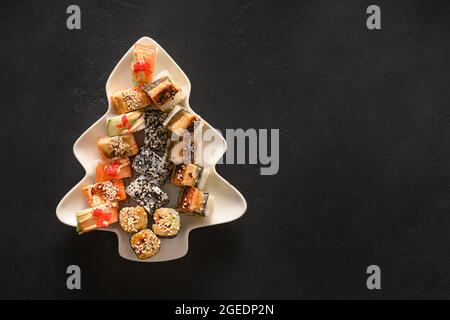 Sushi servi dans un arbre de Noël en forme d'assiette sur fond noir avec espace pour les copies. Vue de dessus. Banque D'Images