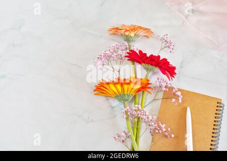 Une composition en holliday avec un bouquet de gerberas colorés avec un carnet, un stylo et un foulard léger en mousseline. Carte de vœux fleurs avec emplacement pour le texte Banque D'Images