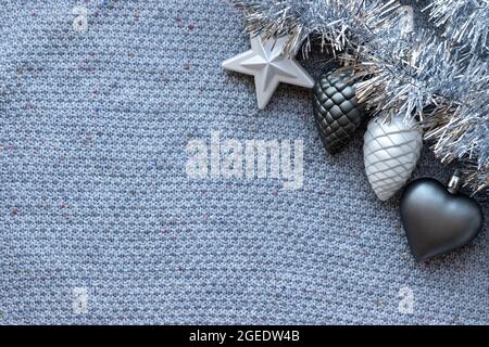 Fond tricoté gris avec guirlande argentée et jouets d'arbre de Noël : coeur, étoile et cônes de pin Banque D'Images