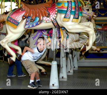 Petits canards de garçon en dessous d'un beau cheval de carrousel qu'il a choisi pour faire le tour sur le joyeux. Il est heureux de sourire avec enthousiasme. Banque D'Images