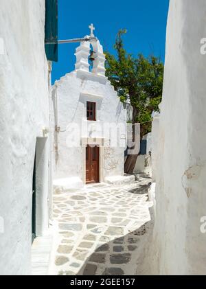 Architecture traditionnelle des Cyclades de l'ancienne chapelle grecque orthodoxe blanchie à la chaux avec beffroi pavés vide étroite rue vide jour d'été cosmope Banque D'Images