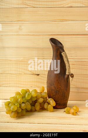 Carafe à raisin sur fond naturel en bois. Style rétro rustique. Pichet d'argile antique avec vin. Raisins verts mûrs juteux de la récolte d'automne. Le concept o Banque D'Images