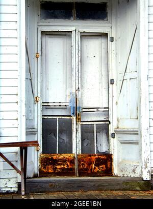 Vieux bois, magasin de pays a des portes doubles avec des protecteurs d'écran et la publicité rouillée au fond. Le magasin est blanc avec l'ancien banc en bois. Banque D'Images