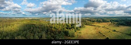 Forêt avec des taches de lumière du soleil et de petits villages sous un ciel bleu nuageux. Grand paysage panoramique aérien Banque D'Images