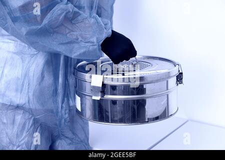 Personne debout dans un laboratoire tenant un autoclave boîte métallique de stérilisateur portant un uniforme de protection. Ton bleu Banque D'Images