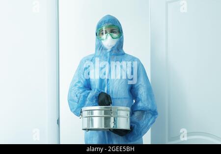 Personne debout dans un laboratoire tenant un autoclave boîte métallique de stérilisateur portant un uniforme de protection. Ton bleu Banque D'Images