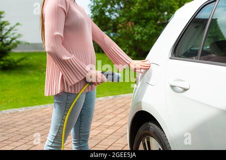 Une femme charge la voiture électrique à la maison avec le câble. Banque D'Images