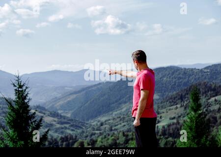 L'homme pointe sa main vers les montagnes. L'homme méconnaissable à l'arrière se tient devant le paysage de montagne et le ciel bleu Banque D'Images