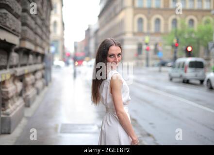 Mise au point sélective d'une belle femme dans une robe blanche, regardant au-dessus de son épaule dans une rue Banque D'Images