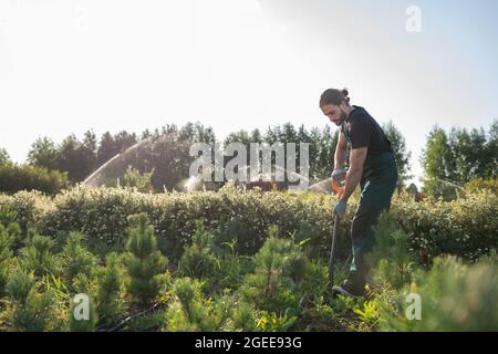 Homme barbu creusant le sol avec une pelle tout en travaillant à la ferme le jour de l'été Banque D'Images