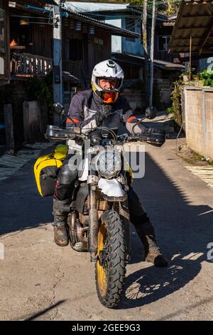 Homme s'arrêtant sur la route avec sa moto dans le village thaïlandais Banque D'Images