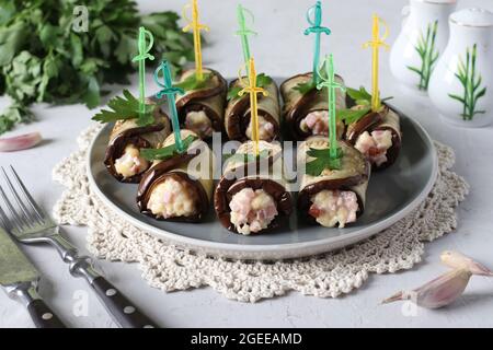 Des petits pains d'aubergines au jambon et au fromage sur une assiette sur fond gris clair. Gros plan Banque D'Images