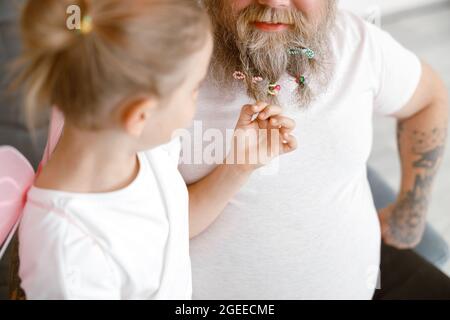 Curieuse petite fille touche la barbe de papa avec des escrocs colorés jouant ensemble à la maison Banque D'Images