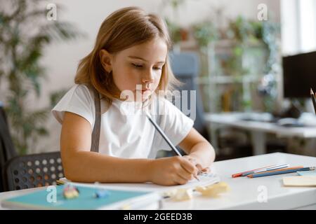 Une petite fille écrit dans un ordinateur portable pour faire ses devoirs au bureau dans une pièce lumineuse Banque D'Images