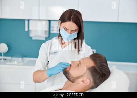 Femme avec masque fait l'injection à l'homme d'âge moyen à la procédure de remplissage de pli nasolabial dans la clinique Banque D'Images