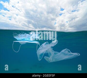 Pollution plastique sous l'eau, masque facial de protection et gants sous la mer avec ciel nuageux, vue fractionnée sous la surface de l'eau, pandémie COVID-19 Banque D'Images