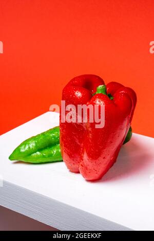 Photographie d'un poivron rouge et d'un poivron vert italien sur un bois blanc et un fond rouge. La photo est prise d'un point de vue supérieur et en position verticale FO Banque D'Images