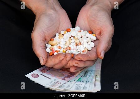 Une poignée de différentes pilules dans les mains des femmes sur fond noir et l'argent russe Banque D'Images