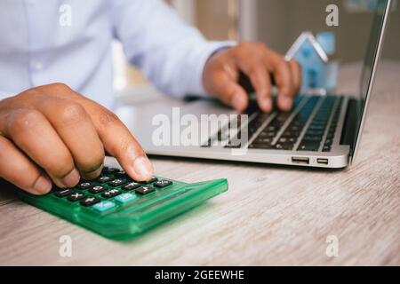 Gros plan sur les mains d'un homme en utilisant une calculatrice et des types sur son ordinateur portable avec un arrière-plan flou Banque D'Images