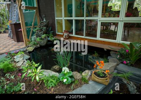 Jardin paysagé avec plan d'eau / étang à poissons entouré d'un mur en briques décoratif et de lits de jardin surélevés avec fougères et fleurs colorées, Australie Banque D'Images