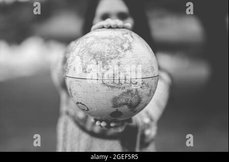 Photo en échelle de gris d'une jeune femme caucasienne tenant une figure de globe Banque D'Images