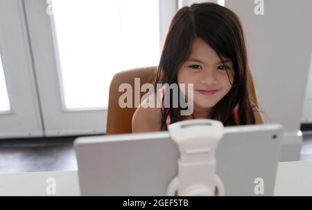 jeune fille biraciale souriante étudiant à la maison pendant la quarantaine coviale Banque D'Images