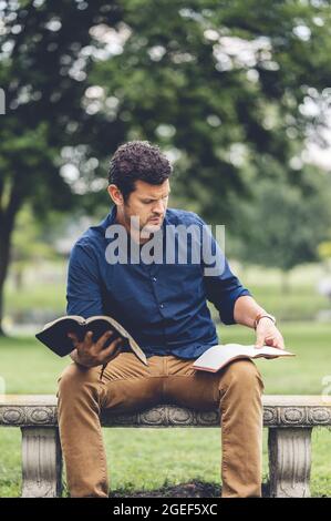 Plan vertical d'un jeune homme caucasien lisant la Bible tout en étant assis sur un banc Banque D'Images