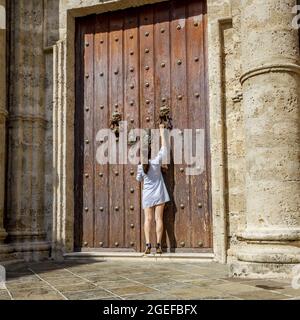 Brunette femme frappant sur une porte de château en bois avec un bouton d'époque Banque D'Images